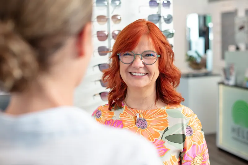 Lächelnde Kundin mit Brille im Gespräch bei Held Hören & Sehen